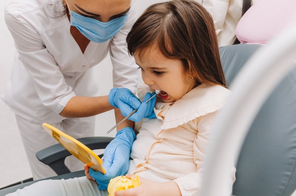 Young girl getting a dental checkup while distracted by a mirror in the dentist's office.