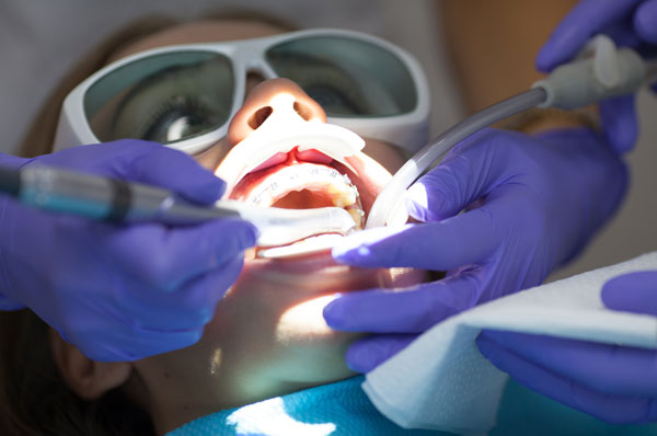 Dental patient receiving treatment with suction and dental instruments, wearing protective glasses.